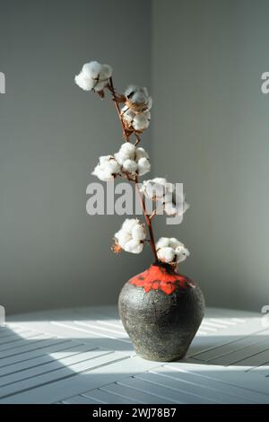 Baumwollblumen in einer Vase auf dem weißen Holztisch in der Minimal-Küche. Wunderschönes Sonnenlicht, perfektes Bild, minimaler Lebensstil. Schwarze Keramikvase hochwertige Fotos Stockfoto