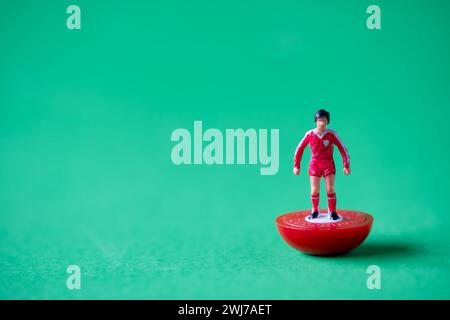 Eine einzelne Subbuteo Minifigur in den Farben der Liverpool FC Heimmannschaft mit rotem Hemd, roten Shorts und roten Socken. Stockfoto