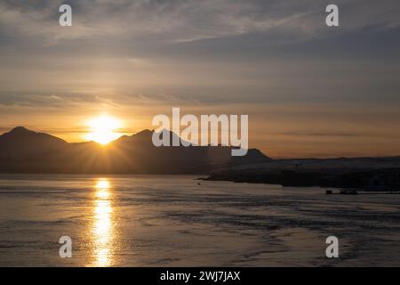 Die Sonne untergeht hinter den Bergen und wirft ein goldenes Spiegelbild auf das stille Wasser der Arktis. Stockfoto