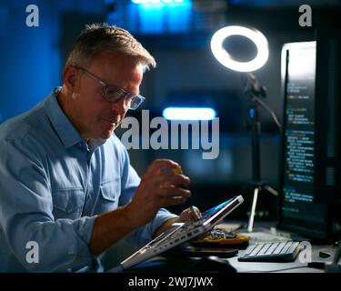 Ausgereifter Elektronikexperte, Der Laptop In Der Werkstatt Mit Niedriger Tastenbeleuchtung Repariert Stockfoto