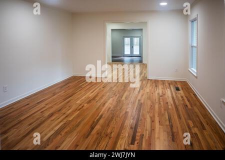 Ein Haus zum Verkauf mit einem leeren weißen Wohnzimmer mit einem doppelten breiten Eingang zum Esszimmer eines neu renovierten und bemalten Hauses mit Dunkelheit Stockfoto