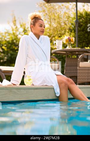 Frau Im Bademantel Sitzt Draußen Und Sitzt Mit Füßen Im Swimmingpool Mit Einem Drink Am Spa Day Stockfoto