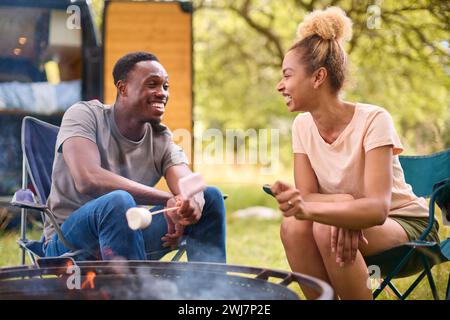 Paare Camping auf dem Land mit Wohnmobil, das Marshmallows im Freien auf Feuer toast Stockfoto