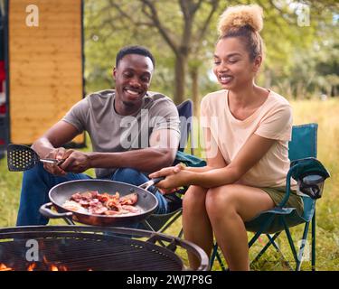 Paare Camping auf dem Land mit RV-Speck und Eiern zum Frühstück draußen am Feuer Stockfoto