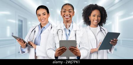 Drei lächelnde Ärztinnen in weißen Labormänteln und blauen Hemden Stockfoto