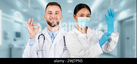 Ein männlicher Arzt gibt ein OK-Zeichen und eine Ärztin trägt eine chirurgische Maske Stockfoto