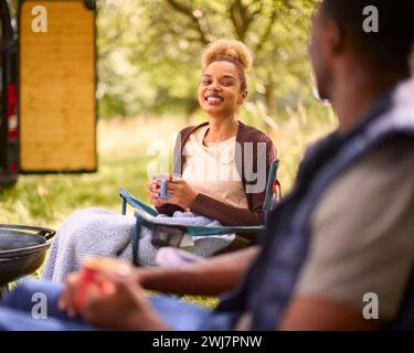 Paare Camping auf dem Land mit Wohnmobil auf Stühlen und Kaffee am Kamin im Freien Stockfoto