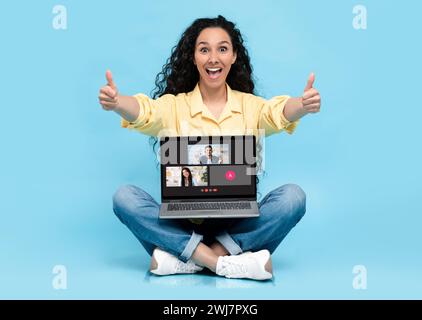 Eine fröhliche junge Frau in einem gelben Hemd gibt sich beim Sitzen die Daumen hoch Stockfoto