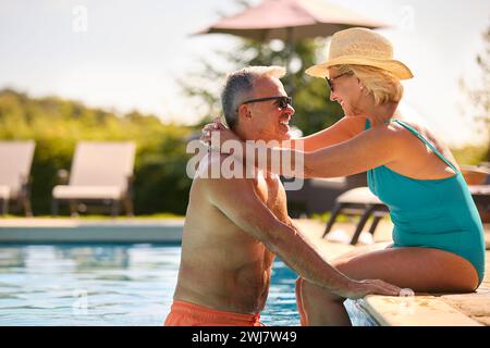 Liebevolles Seniorenpaar Im Urlaub In Badekleidung, Entspannend Am Hotel Swimmingpool Stockfoto