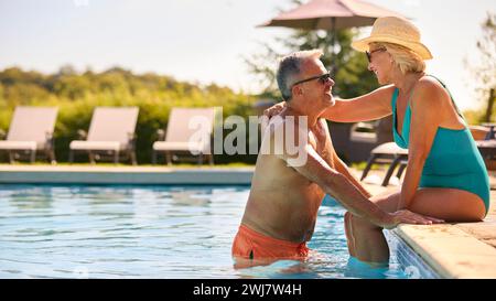 Liebevolles Seniorenpaar Im Urlaub In Badekleidung, Entspannend Am Hotel Swimmingpool Stockfoto