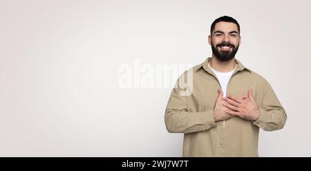 Ein glücklicher, selbstbewusster, gutaussehender junger Mann aus dem Nahen Osten mit einem Bart in lässiger Form, die Hände an die Herzbrust gelegt hat Stockfoto
