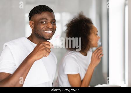 Glückliches schwarzes Paar beschäftigt sich mit Mundpflege und putzt die Zähne drinnen Stockfoto