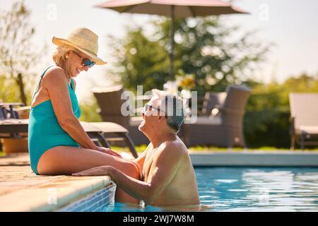 Liebevolles Seniorenpaar Im Urlaub In Badekleidung, Entspannend Am Hotel Swimmingpool Stockfoto