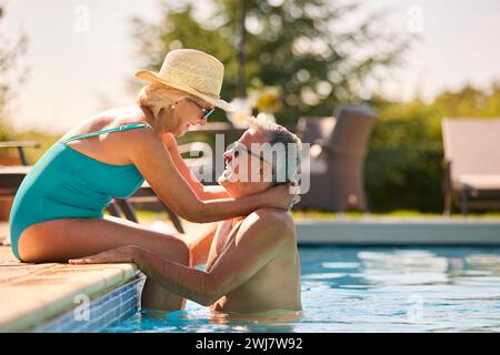 Liebevolles Seniorenpaar Im Urlaub In Badekleidung, Entspannend Am Hotel Swimmingpool Stockfoto