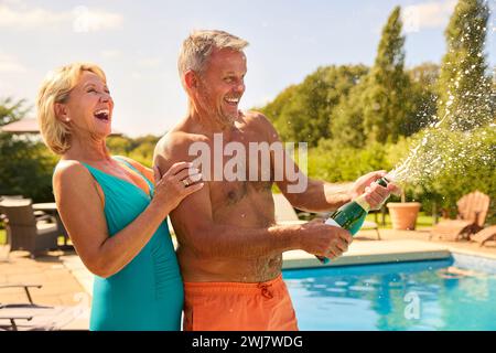 Seniorenpaar Im Urlaub In Badekleidung, Eröffnung Champagner Am Hotel Swimming Pool Stockfoto