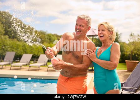 Seniorenpaar Im Urlaub In Badekleidung, Eröffnung Champagner Am Hotel Swimming Pool Stockfoto