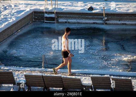 Mann, der an einem sonnigen Wintertag im Stadtteil Katajanokka in Helsinki, Finnland, vorbei an einem gefrorenen Meerwasserpool im Allas Sea Pool, einem Meeresbad und lido, spaziert Stockfoto