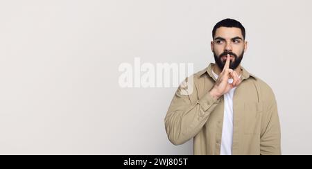Ernstzunehmender, gutaussehender junger Mann aus dem Nahen Osten mit Bart in lässiger Weise, machen Shhh-Geste mit Fingerschlippen Stockfoto
