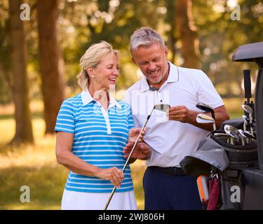 Senior Pärchen Neben Buggy Auf Dem Golfplatz, Die Gemeinsam Clubs Auswählen Stockfoto