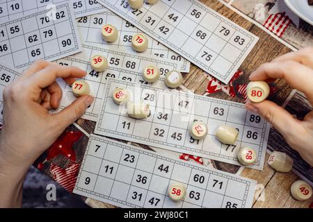 Lottospiel spielen. Person, die den Würfel mit der Figur auf dem Hintergrund der Bingo-Karte hält. Nostalgie Lifestyle. Tischspiele. Retro-Spiele. Zylinder mit Zahlen. Stockfoto