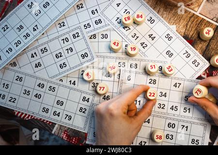 Lottospiel spielen. Person, die den Würfel mit der Figur auf dem Hintergrund der Bingo-Karte hält. Nostalgie Lifestyle. Tischspiele. Retro-Spiele. Zylinder mit Zahlen. Stockfoto