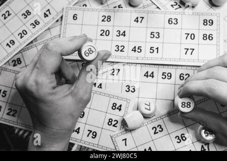 Lottospiel, schwarz-weiß. Person, die den Würfel hält, mit Figur auf Bingo-Kartenhintergrund, monochrom. Nostalgie Lifestyle. Tischspiele. Stockfoto