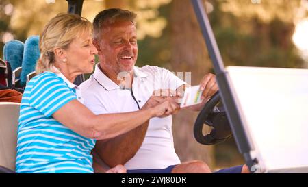 Senior Pärchen Sitzen Im Buggy Auf Dem Golfplatz Und Markieren Gemeinsam Die Punktekarte Stockfoto