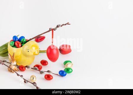 Rotes Osterei hängt an einem Weidenzweig mit Tulpen und Schokoladeneiern, weißer Hintergrund, Kopierraum Stockfoto