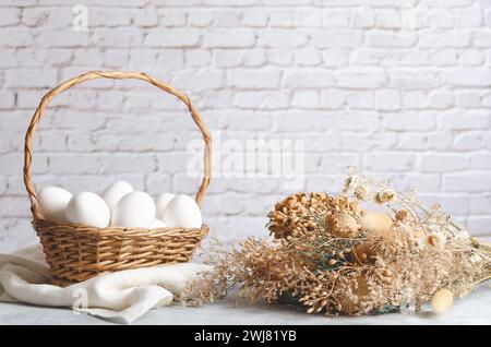 Ein Korb mit weißen Hühnereiern auf hellem Hintergrund mit getrockneten Blumen. Vorderansicht mit Kopierraum. Stockfoto