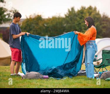Junges Paar, Das Zelt Beim Sommermusikfestival Aufstellt Und Campingausrüstung Auspackt Stockfoto