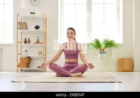 Porträt einer entspannten jungen Frau, die zu Hause Yoga-Übungen macht und in Lotusposition sitzt. Stockfoto