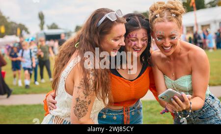 Drei Weibliche Freunde Mit Glitzer Und Blick Auf Das Handy Beim Summer Music Festival Stockfoto