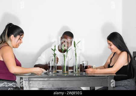 Drei junge Latino-Freunde sitzen im Speisesaal und reden und lächeln, während sie ihr Mittagessen essen Stockfoto