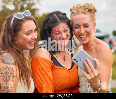 Drei Weibliche Freunde Mit Glitzer Und Blick Auf Das Handy Beim Summer Music Festival Stockfoto