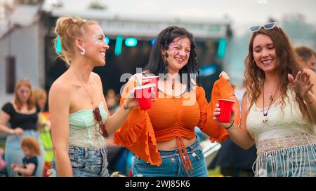 Drei Weibliche Freunde Tragen Glitzertanz Beim Summer Music Festival Und Halten Drinks Stockfoto