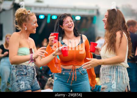 Drei Weibliche Freunde Tragen Glitzertanz Beim Summer Music Festival Und Halten Drinks Stockfoto
