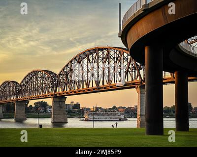 Das Flussboot Belle of Louisville schwimmt während des Sonnenuntergangs unter der Big Four Bridge auf dem Ohio River in Louisville, Kentucky, USA. Stockfoto