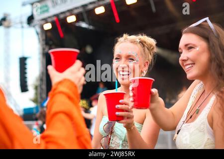 Drei Weibliche Freunde Mit Glitzer, Die Beim Summer Music Festival Spaß Haben Und Getränke Halten Stockfoto