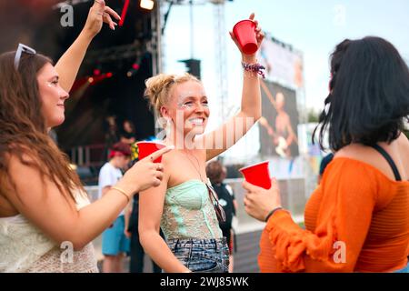 Drei Weibliche Freunde Mit Glitzer, Die Beim Summer Music Festival Spaß Haben Und Getränke Halten Stockfoto