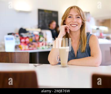 Porträt Einer Lächelnden Frau, Die Am Tisch Im Café Mit Getränk Sitzt Stockfoto