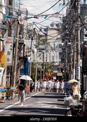 Das tägliche Leben in Japan Eine Szene von Männern in weißen Kostümen, die einen Mikoshi tragen und während eines Sommerfestes in einem Schrein durch die Stadt ziehen. Stockfoto