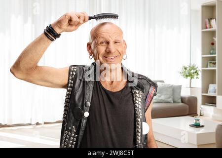 Glatzkopf, der eine Haarbürste über dem Kopf hält und zu Hause lächelt Stockfoto