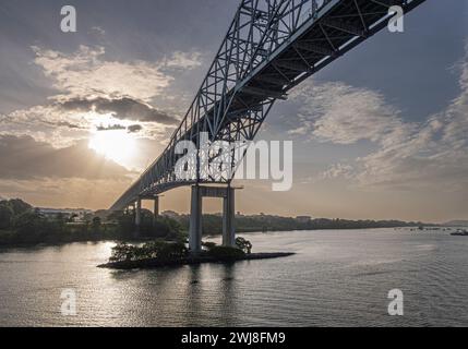 Panamakanal, Panama - 24. Juli 2023: Sonnenaufgang über der Hängebrücke des Amerikas am Eingang. Grüne bewaldete Küste. Stockfoto