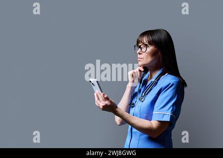 Krankenschwester mit Smartphone, Profilansicht auf grauem Atelierhintergrund Stockfoto