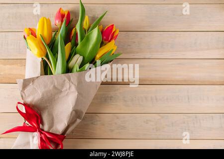 Blumenstrauß aus bunten frischen Tulpen, umhüllt in umweltfreundliches Handwerkspapier. Blumen auf hölzernem Hintergrund. Platz für Text. Stockfoto