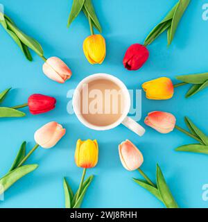 Kreatives Frühlingslayout mit bunten Tulpenblüten und einer Tasse Kaffee auf blauem Hintergrund. Minimales Kaffeekonzept. Trendige Frühlingsblumen-Idee. Stockfoto