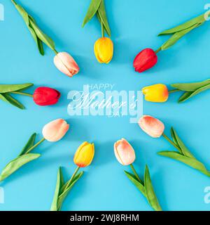 Kreative Frühlingskomposition aus bunten Tulpenblüten mit „Happy Mother's Day“-Text auf blauem Hintergrund. Minimales Muttertagskonzept. Stockfoto