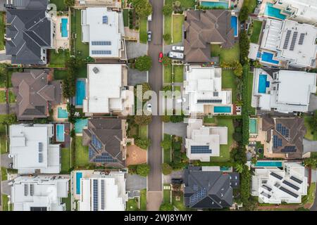 Blick von oben nach unten auf eine Vorstadtstraße, gesäumt von modernen Prestigehäusern mit Pools und Sonnenschirmen auf dem Dach im äußeren Sydney, Australien. Stockfoto