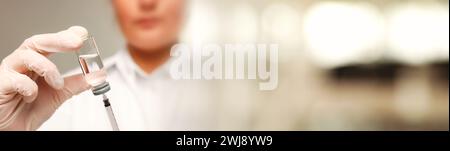 Arzt füllt Spritze mit Medikamenten aus Glasfläschchen auf verschwommenem Hintergrund, Großaufnahme. Bannerdesign Stockfoto