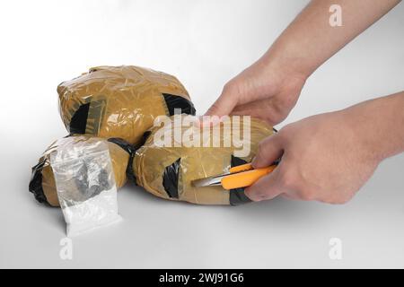 Schmuggel und Drogenhandel. Mann, der ein Paket mit Betäubungsmitteln mit einem Koffer auf weißem Hintergrund öffnet, Großaufnahme Stockfoto